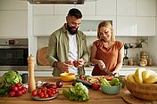 Ein junges Paar schneidet Gemüse für Low-Fodmap-Ernährung Eine junge Frau und ein junger Mann stehen in der Küche und schneiden Gemüse für eine Low-Fodmap-Ernährung